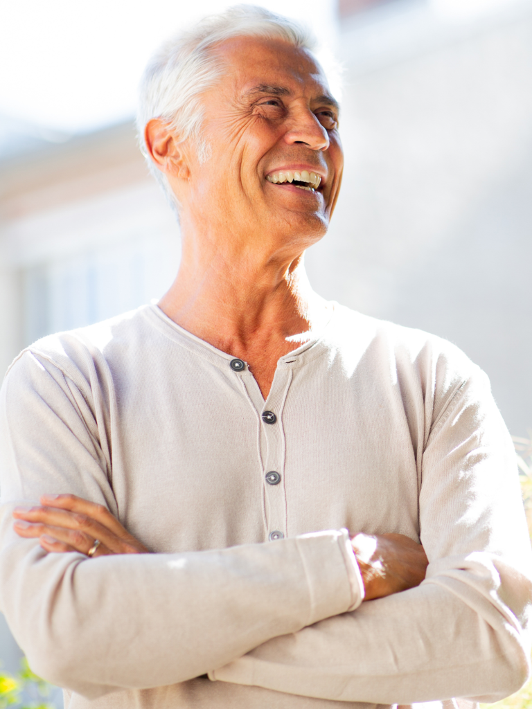 older gentleman in beige shirt folding his arms and smiling